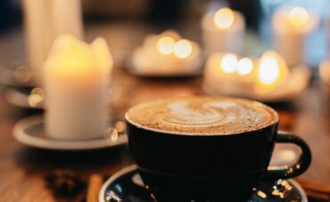 Cozy coffee shop ambiance with a latte on a wooden table surrounded by candles and warm bokeh lights.