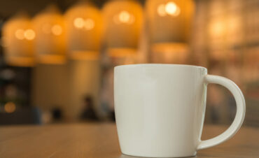 white coffee mug on the wooden table in the coffee shop with cozy atmosphere